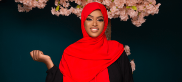 Woman in a red hijab and black abaya standing before pink cherry blossoms