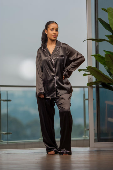 Woman wearing black satin pajama set on balcony with glass railing and green plant
