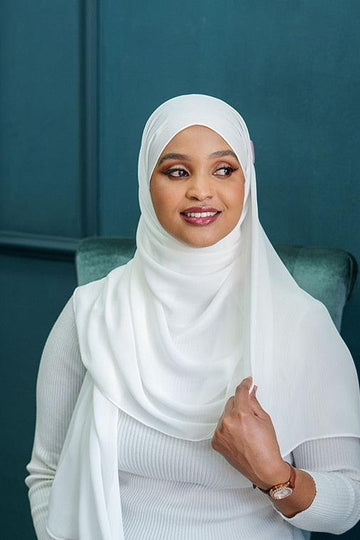 Woman wearing elegant white crepe chiffon hijab and modest clothing, seated indoors