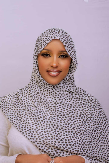 Smiling woman wearing a white polka dot hijab and modest clothing, studio background